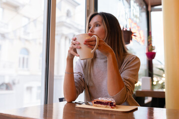 Woman with blonde hair sips cappuccino in a cafe. She is holding the glass up to her face, taking a...