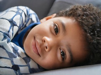 African american child wearing pajamas, laying on a coach, watching cartoons