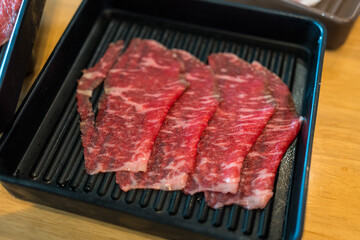 Premium thinly sliced ​​beef in black tray on wood table