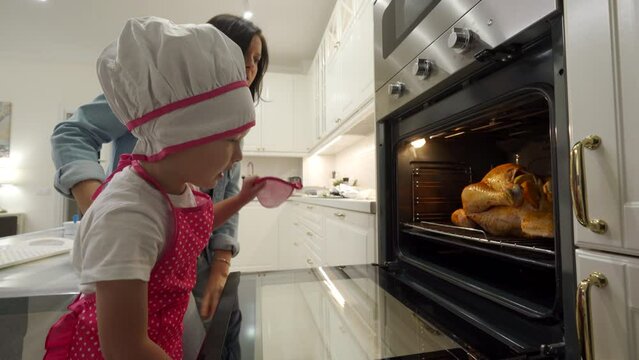 mother and child cooking roasted stuffed turkey in kitchen oven, thanksgiving and christmas holiday dinner