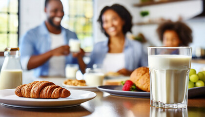 Close-up of a glass of milk and a croissant on the table with family in the background - obrazy, fototapety, plakaty