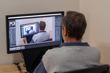 Mature Caucasian man sitting at a desk of a home office working on a picture within picture on a...