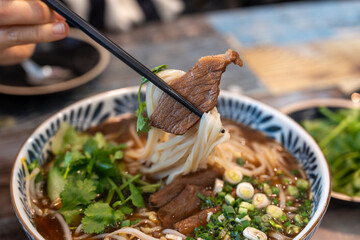 Closeup photo of beef rice noodle (pho) held in chopsticks, taken in a restaurant