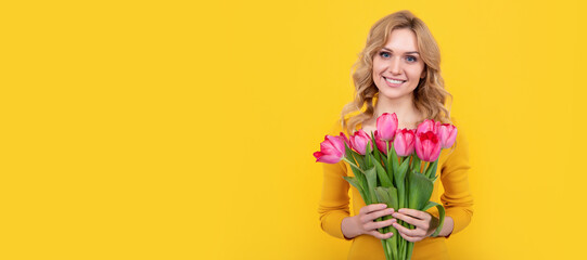 happy young blond woman with spring tulip flowers on yellow background. Woman isolated face...