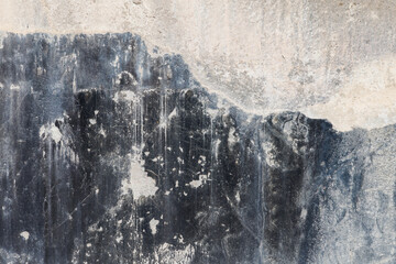 old concrete wall with black paint leftovers covered with whitewash stains, full-frame background...