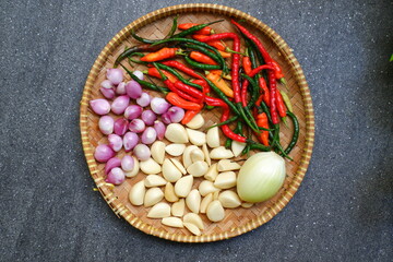 Top view of garlic, shallot and onion and chilies in a bamboo tray