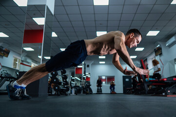 Muscular shirtless man doing push-ups in a jump in the gym. 
