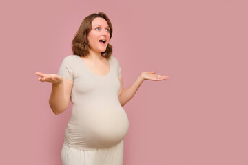 An enthusiastic pregnant woman on a studio pink background. Pregnancy in a happy woman with a...