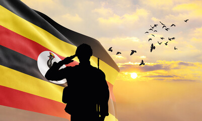 Silhouette of a soldier with the Uganda flag stands against the background of a sunset or sunrise....