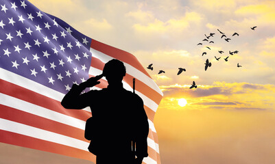 Silhouette of a soldier with the USA flag stands against the background of a sunset or sunrise....