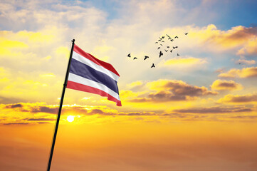 Waving flag of Thailand against the background of a sunset or sunrise. Thailand flag for Independence Day. The symbol of the state on wavy fabric.