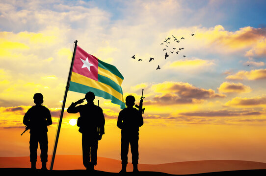 Silhouettes of soldiers with the Togo flag stand against the background of a sunset or sunrise. Concept of national holidays. Commemoration Day.