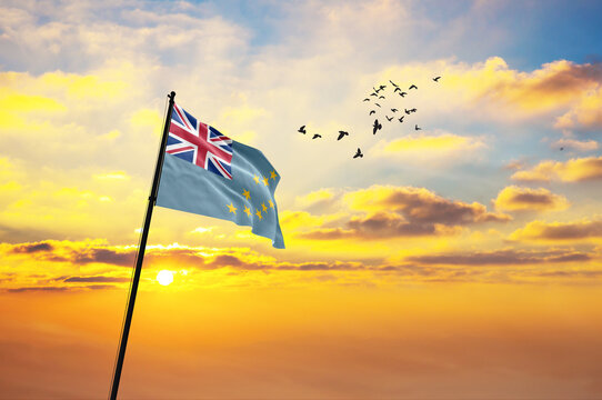 Waving flag of Tuvalu against the background of a sunset or sunrise. Tuvalu flag for Independence Day. The symbol of the state on wavy fabric.