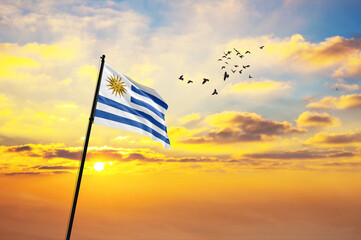 Waving flag of Uruguay against the background of a sunset or sunrise. Uruguay flag for Independence Day. The symbol of the state on wavy fabric.