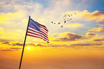 Silhouette of a soldier with the USA flag stands against the background of a sunset or sunrise....