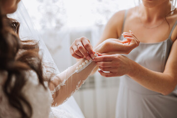 Morning of the bride. The bride's maid of honor helps the bride lace up her dress, fasten buttons on the dress or sleeves. Girlfriends help the bride fasten her dress - Powered by Adobe