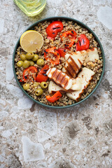 Quinoa with slices of grilled halloumi, bell pepper and green olives, top view on a light-brown granite background, vertical shot with space