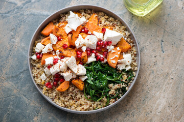 Quinoa with feta, roasted sweet potato, pomegranate and wilted spinach, horizontal shot on a grey...