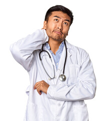 Young Chinese man as a medical doctor in studio touching back of head, thinking and making a choice.