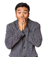 Young Chinese man in studio background shocked, covering mouth with hands, anxious to discover something new.