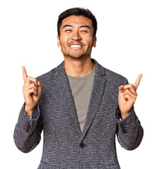 Young Chinese man in studio background indicates with both fore fingers up showing a blank space.
