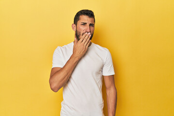 Young Hispanic man on yellow background yawning showing a tired gesture covering mouth with hand.