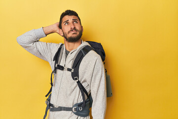 Young Hispanic man ready for hiking touching back of head, thinking and making a choice.