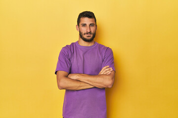 Young Hispanic man on yellow background who feels confident, crossing arms with determination.