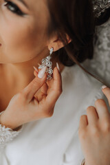 close-up of a beautiful girl in soft satin underwear wearing earrings. Wedding morning of the...