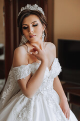 fashion photo of a beautiful bride with dark hair in an elegant wedding dress and stunning makeup in the room on the morning of the wedding. The bride is preparing for the wedding