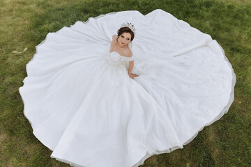 brunette bride in off-the-shoulder lace white dress and tiara posing with a bouquet of white and...