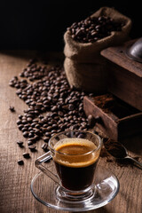 In the background, coffee beans and ground coffee, in the foreground an espresso in a glass cup