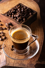 In the background the coffee beans, in the foreground an espresso in a glass cup - 700973362