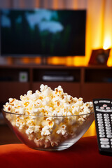 Popcorn in a glass bowl and TV remote control.