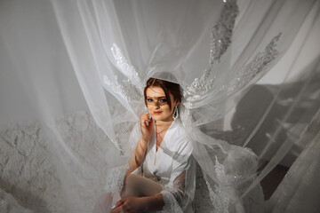 Nice cute girl in a boudoir robe. Happy beautiful bride under veil. Fashion, beauty, style. Morning of the bride. Beautiful bride with stylish make up and hair style.