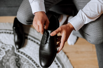 An elegant man wears black leather formal shoes. Tying shoes. Business man tying shoelaces on the floor. Up close The groom is preparing for the wedding. - obrazy, fototapety, plakaty