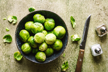 Frischer Rosenkohl in einer Schüssel und Salz und Pfefferstreuer auf einem grünen Tisch....