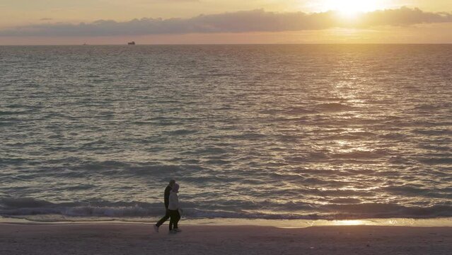 Slow motion footage of adult couple walking at distance on a beach at sunset. 4k, h265, 30 fps, 4:2:2 10 bit (BT709)