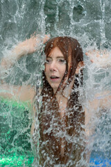 beautiful young cute sexy Portrait of a redhead woman with raised arms under the splashing pattering waterfall burbling water
