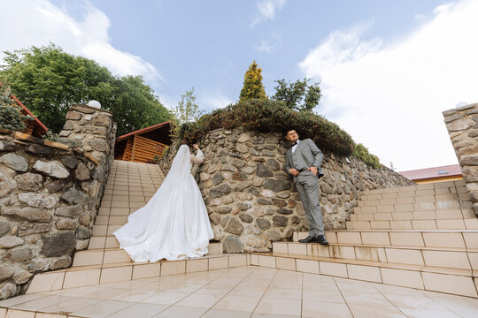 wide-angle photo of the bride and groom on the steps against the background of stone walls. Free space.