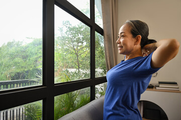 Happy retired woman in sportswear doing stretching exercises at home. Sports and Healthy lifestyle concept.