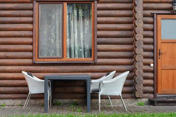 Rattan chairs and a table next to the wooden log house outdoors.