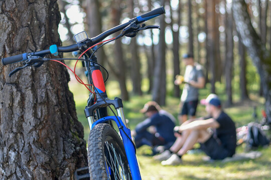 Close up of a bicycle in the forest with blurred background of unidentified cyclists resting under the tree. Selective focus.