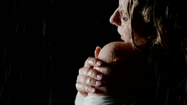 sensual woman standing alone in rain in night, stroking her wet and naked shoulders