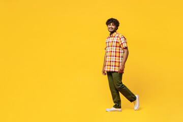 Fototapeta na wymiar Full body side view smiling happy cheerful fun young Indian man he wears shirt casual clothes walking going looking camera isolated on plain yellow color background studio portrait. Lifestyle concept.