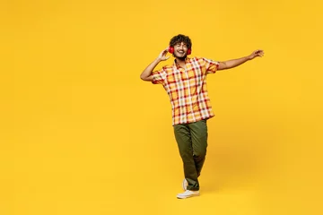 Foto op Canvas Full body young cheerful fun happy cool Indian man he wearing shirt casual clothes dancing listen to music in headphones isolated on plain yellow color background studio portrait. Lifestyle concept. © ViDi Studio