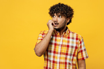 Young minded pensive confused puzzled Indian man wears shirt casual clothes biting nails fingers look aside on area mock up isolated on plain yellow color background studio portrait Lifestyle concept - obrazy, fototapety, plakaty