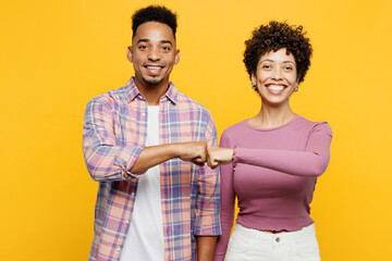 Young happy couple two friends family man woman of African American ethnicity wearing purple casual clothes together look camera do fist bump gesture isolated on plain yellow orange background studio.