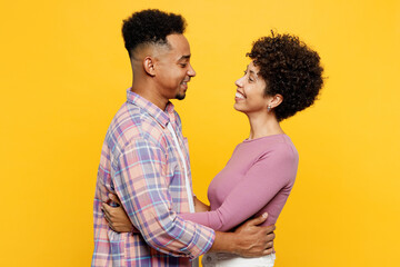 Side view young happy couple two friend family man woman of African American ethnicity wearing purple casual clothes together hug cuddle embrace look to each other isolated on plain yellow background