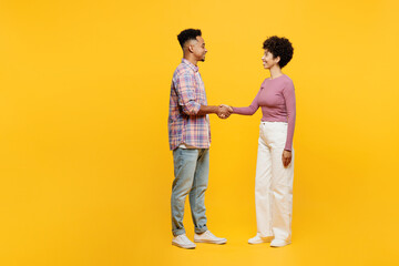 Full body young couple two friends family man woman of African American ethnicity wear casual clothes hold hands folded handshake gesture isolated on plain yellow background. Friendship greet concept. - obrazy, fototapety, plakaty